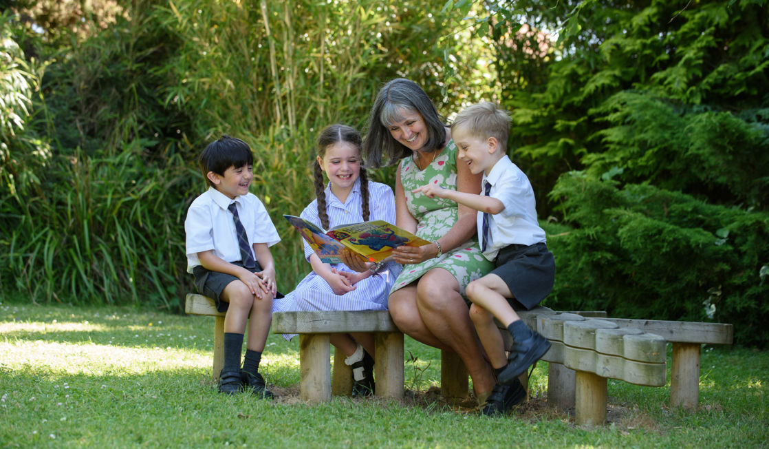 wycliffe teacher and nursery pupils reading a book outdoors