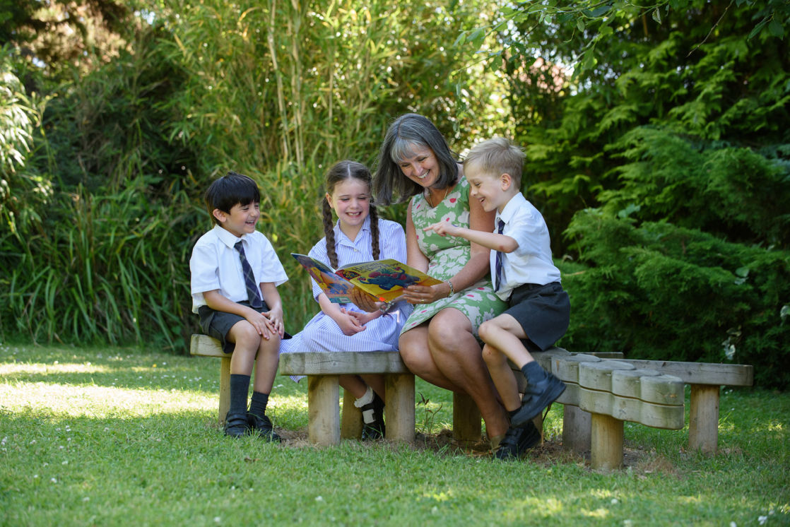 wycliffe teacher and nursery pupils reading a book outdoors