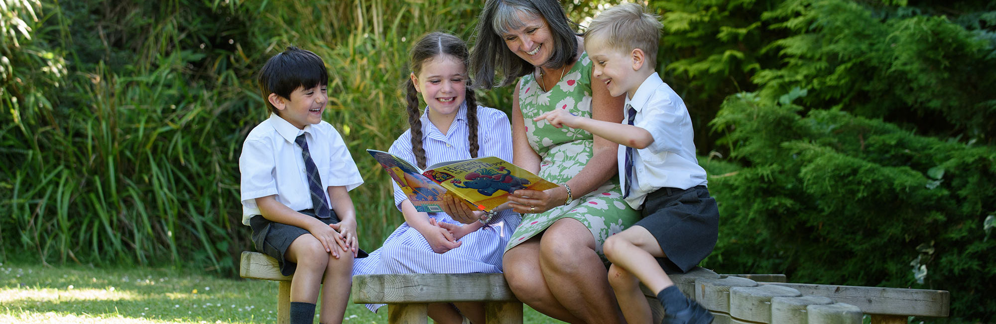 wycliffe teacher and nursery pupils reading a book outdoors